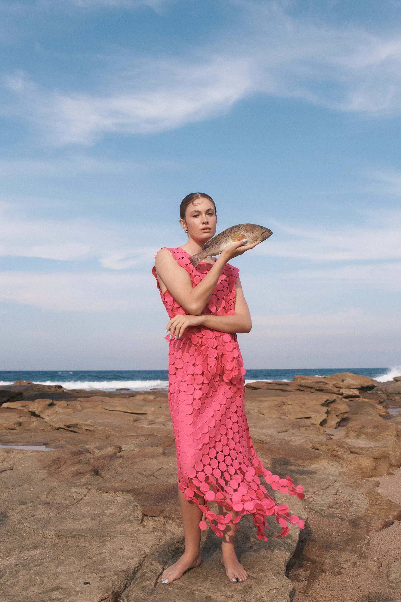 Woman in a pink dress holding a fish on a rocky coastline