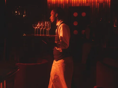 Server carrying drinks through the red-lit Owner’s Office bar