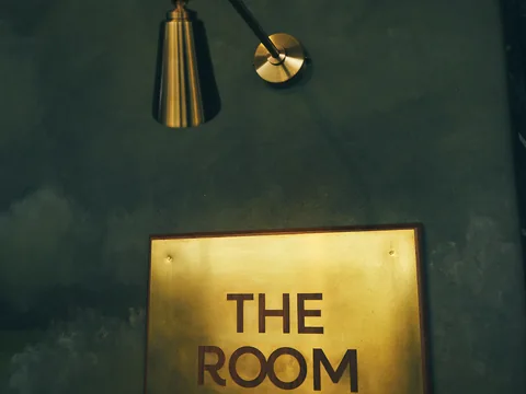 Brass The Room sign on a dark green wall